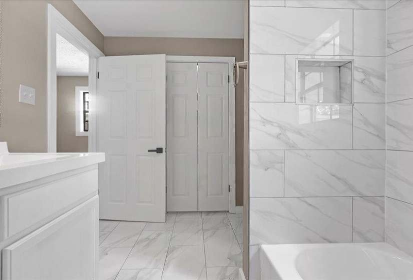 Bathroom featuring large format wall and floor tiling, a built-in shower niche, and a white vanity with panel-style cabinetry