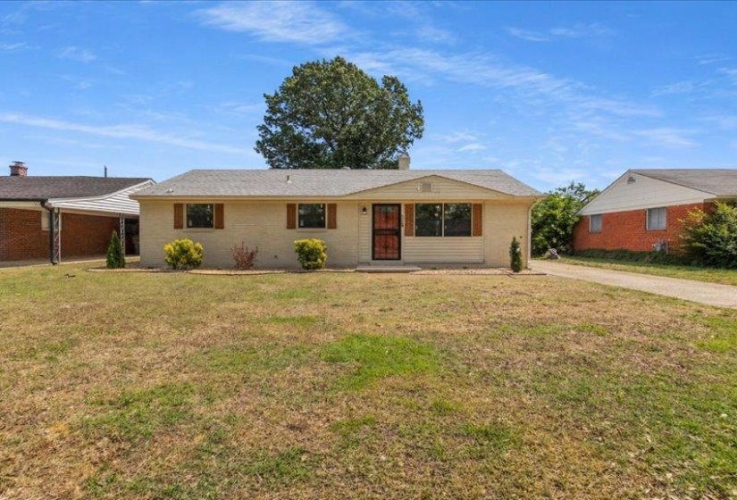 Ranch-style residence featuring a light-colored brick exterior, a dark shingle roof, and decorative window shutters