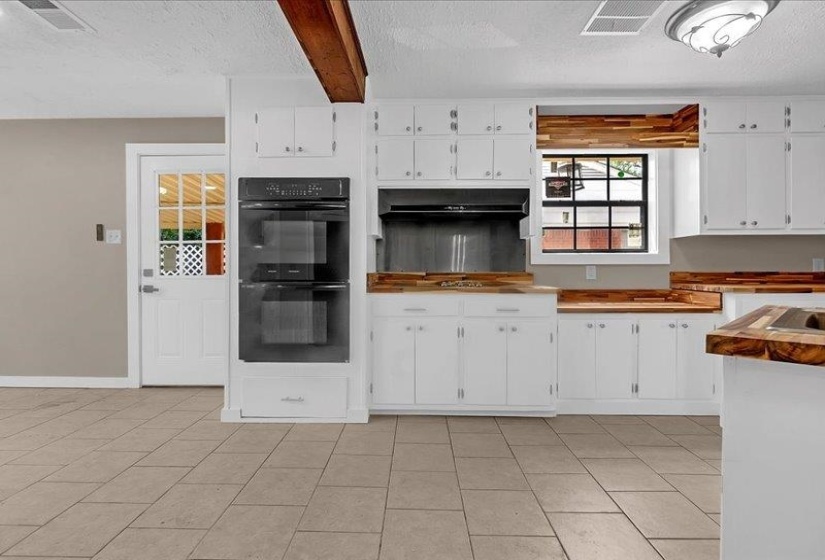 Kitchen featuring white cabinetry, wood-finish countertops, built-in double oven, and tile flooring