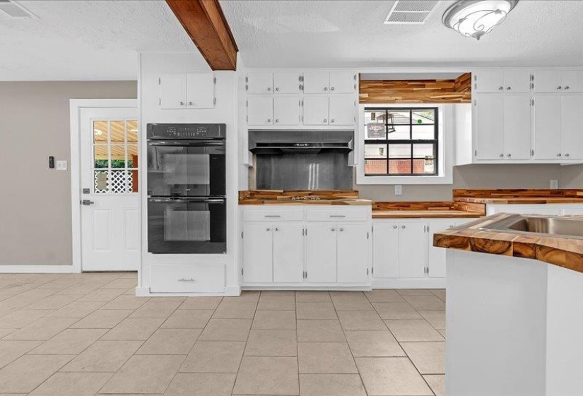 Kitchen featuring white cabinetry, wood-finish countertops, tile flooring, a double wall oven, and exposed wood beam