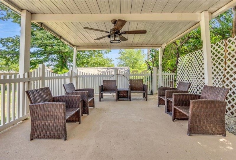 Covered patio featuring a ceiling fan with integrated lighting, a concrete floor, and white slatted fencing
