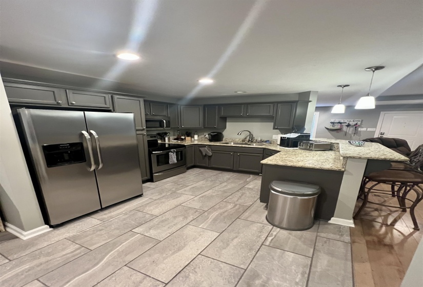 Kitchen featuring a peninsula, appliances with stainless steel finishes, gray cabinetry, a breakfast bar area, and pendant lighting