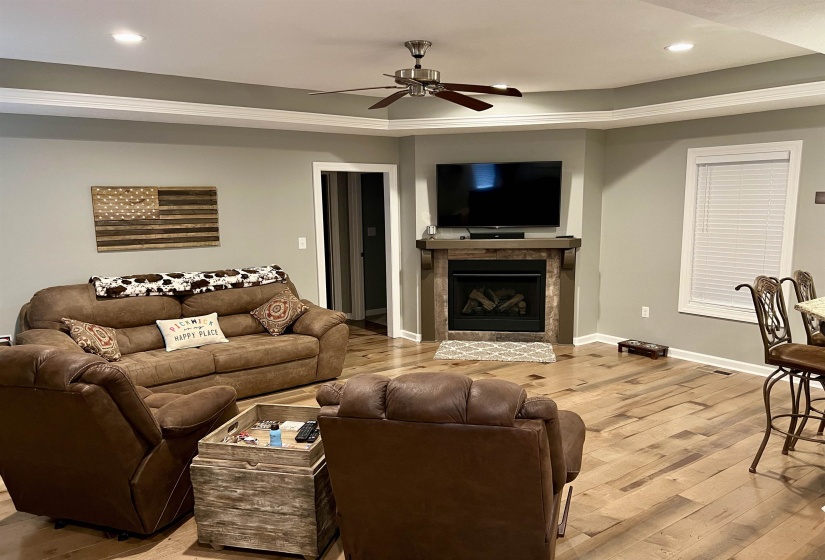Living area with recessed lighting, a glass covered fireplace, light wood-style floors, a raised ceiling, and a ceiling fan