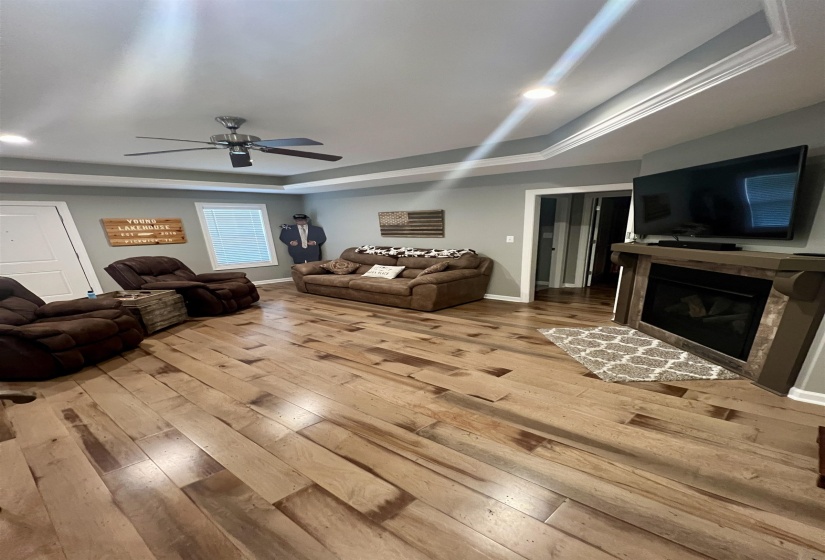 Living room featuring a tray ceiling, light wood finished floors, a glass covered fireplace, ceiling fan, and recessed lighting