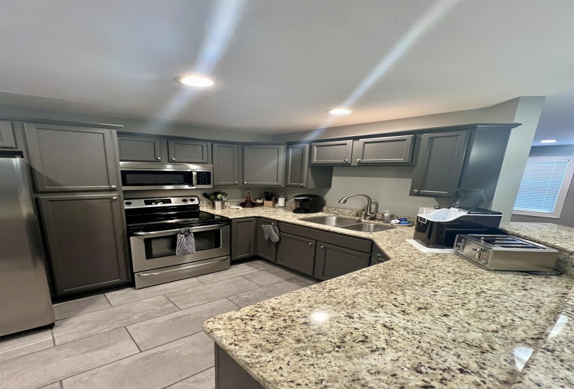 Kitchen featuring stainless steel appliances, gray cabinetry, light stone counters, and recessed lighting