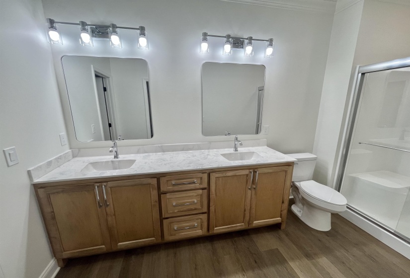 Full bathroom with double vanity, a stall shower, and dark wood finished floors