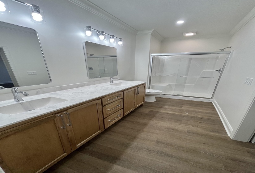 Bathroom featuring a shower stall, double vanity, ornamental molding, dark wood finished floors, and recessed lighting