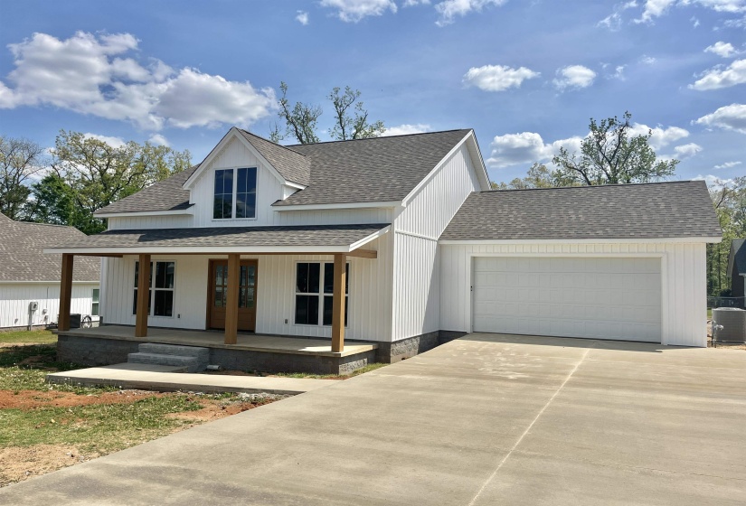 Modern farmhouse featuring roof with shingles, an attached garage, a porch, and driveway