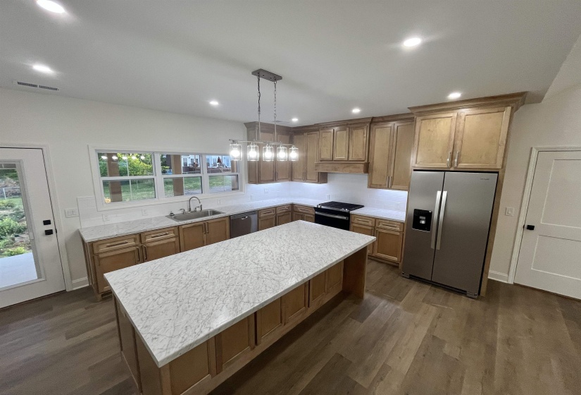 Kitchen featuring stainless steel appliances, dark wood-style floors, wood finish cabinets, and decorative light fixtures