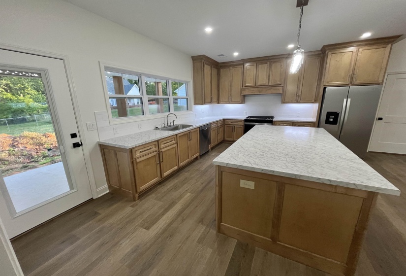 Kitchen with stainless steel appliances, wood finish cabinets, a kitchen island, dark wood-type flooring, and hanging light fixtures