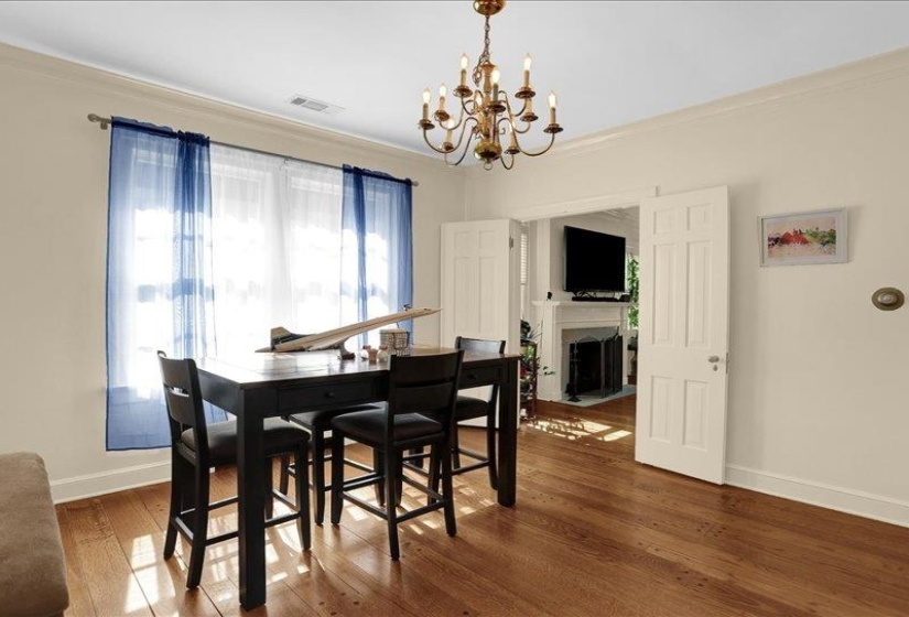 Hardwood flooring extending throughout, featuring a classic chandelier, crown molding, and architectural paneled doors