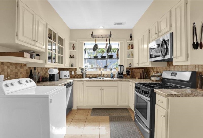 Kitchen featuring light-toned cabinetry, a mosaic tile backsplash, and stone-finish countertops -- how about that window box.  Fresh herbs anyone?