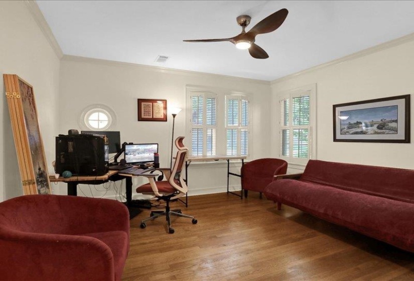 Light-filled room featuring wood-finish flooring, white crown molding, and a modern ceiling fan with integrated lighting
