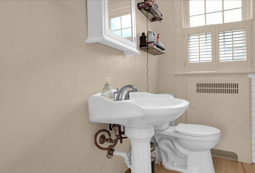 Pedestal sink with chrome faucet, toilet, and window with plantation shutters