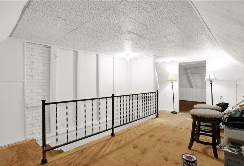 Upper-level landing featuring a black wrought iron railing, white paneled walls, and a white painted brick accent wall
