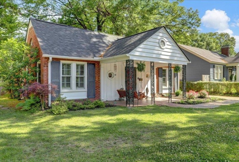 Brick and siding exterior featuring a covered porch with decorative iron columns, a cute arched front window, lovely landscapping and a front load garage.