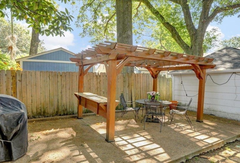 Outdoor patio featuring a wooden pergola with string lights, a built-in wooden bench, concrete slab flooring, and perimeter wood fencing....just invite some friends and some burgers!