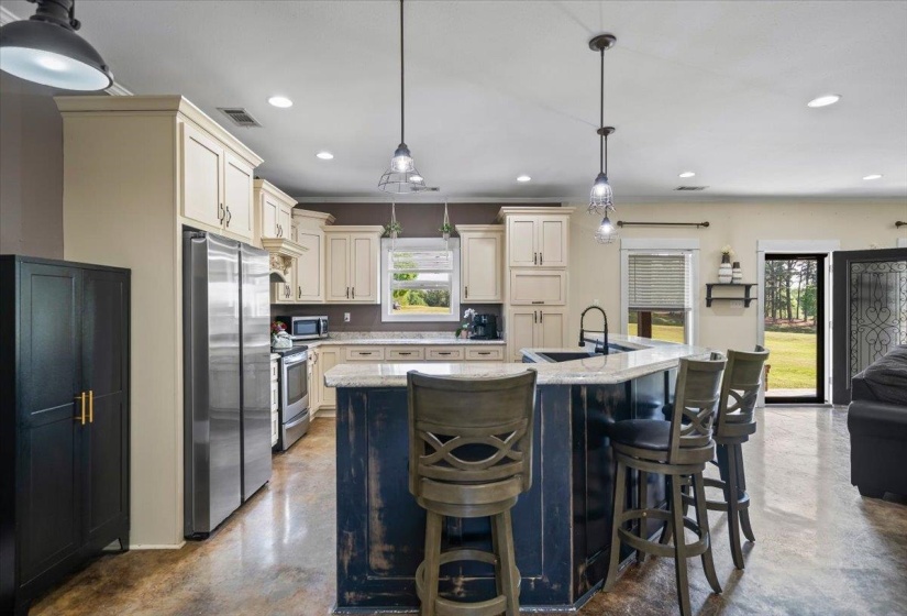 Spacious kitchen featuring an expansive island with seating, pendant lighting, stainless steel appliances, and light-toned cabinetry