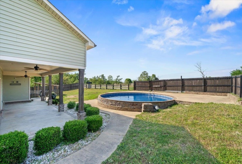 Expansive outdoor living area featuring a covered patio with ceiling fans, a concrete walkway, and a round, stone-clad swimming pool