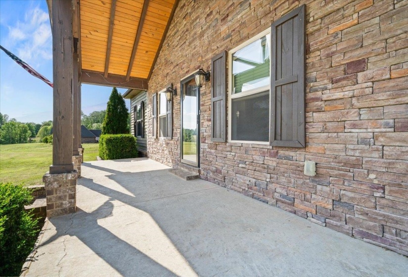 Spacious covered porch with a natural stone facade, wood-plank ceiling, and sturdy structural columns
