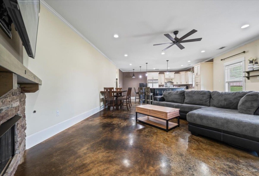 Open-concept living area featuring stained concrete flooring, a stone-front fireplace with a wood mantle, and recessed lighting