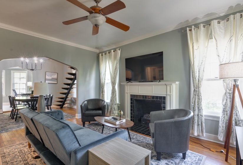 Living room featuring a decorative fireplace with a white mantel and dark tiled surround, hardwood-finish flooring, two large windows, and an arched entryway