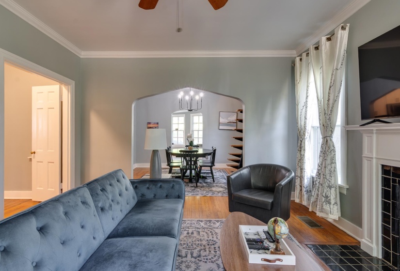 Living area featuring hardwood-finish flooring, a fireplace with a tiled surround, a decorative mantelpiece, and a cased archway opening to an adjacent room