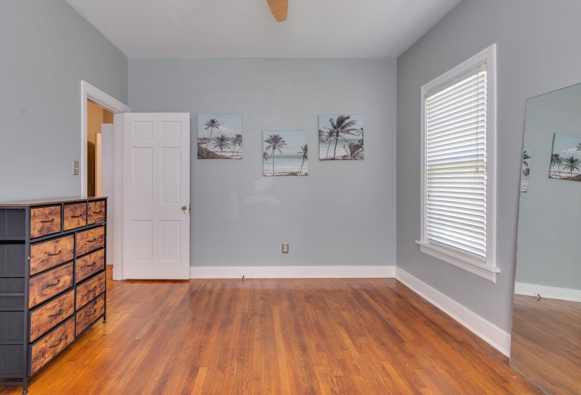 Hardwood flooring throughout featuring white baseboards, a white paneled door, and a single window with white blinds