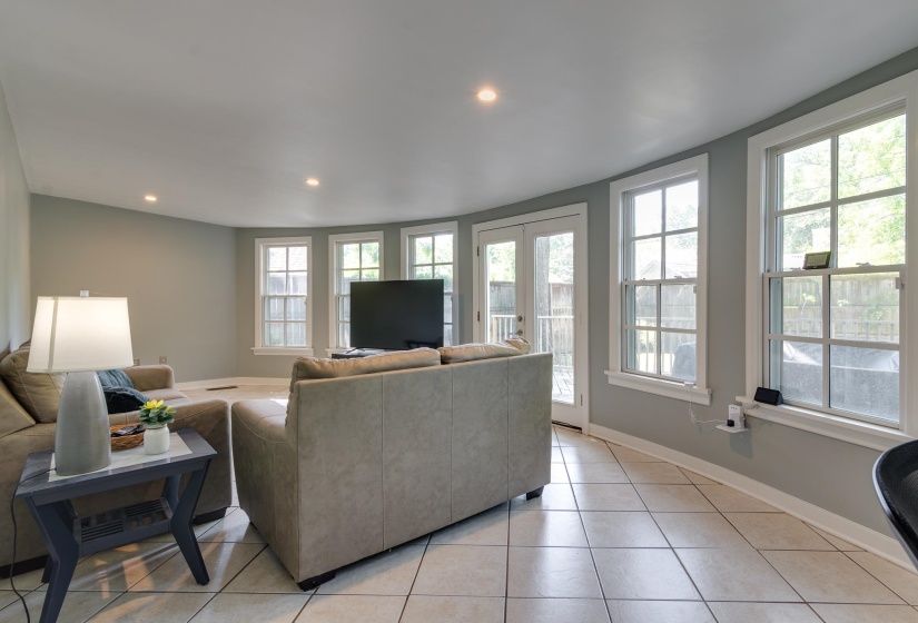 Spacious living area featuring light-toned tile flooring, recessed lighting, multiple large windows with white trim, and a set of French doors