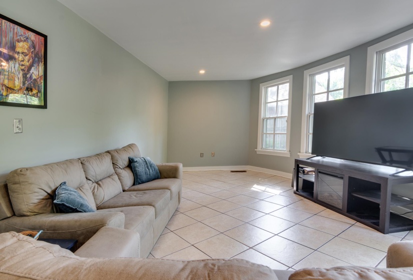 Spacious living area featuring light-toned tile flooring, recessed lighting, and multiple windows with white trim