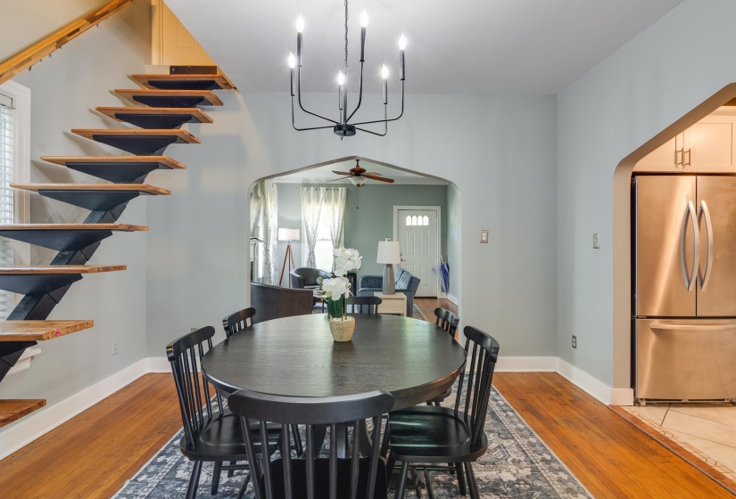 Hardwood flooring extending through an arched entryway, featuring a modern chandelier and open riser staircase