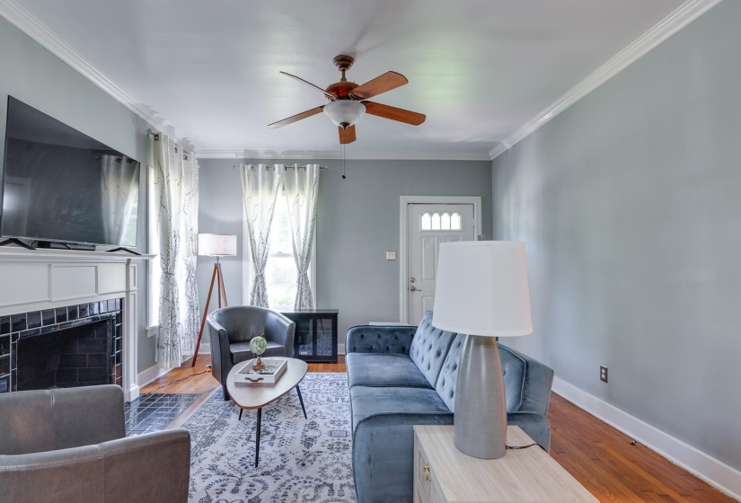 Living area featuring wood-finish flooring, a white mantel, black tile fireplace surround, and crown molding