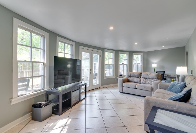 Spacious living area featuring light-toned tile flooring, recessed lighting, and multiple large windows with white trim