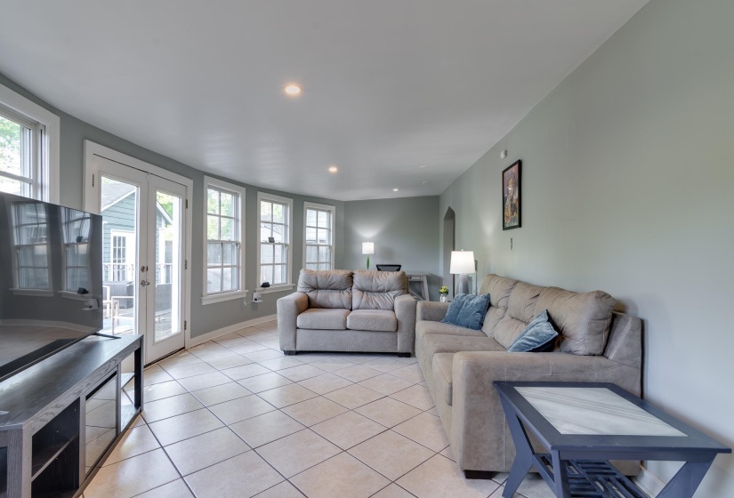 Spacious living area featuring light-toned tile flooring, recessed lighting, double French doors, and multiple windows with white trim