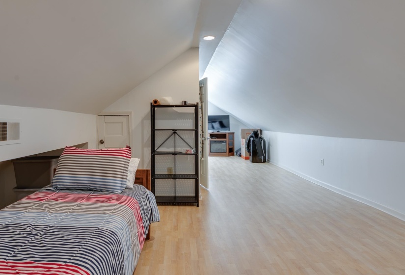 Attic space featuring wood-finish flooring, sloped ceilings, a built-in air vent, and a white interior door
