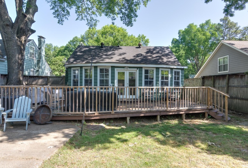Rear exterior featuring an elevated wood deck with white French doors, multiple windows, and a dark shingle roof