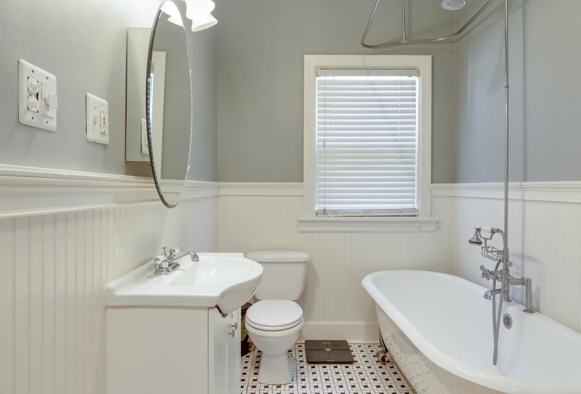 Bathroom featuring a freestanding clawfoot tub with shower attachment, beadboard wainscoting, a wall-mounted sink with chrome faucet, a round mirror, and black-and-white mosaic tile flooring