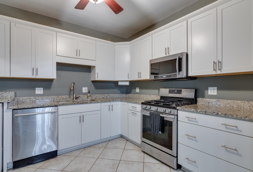Kitchen featuring white cabinetry, light-toned countertops, stainless steel appliances including a gas range and microwave, and tile flooring