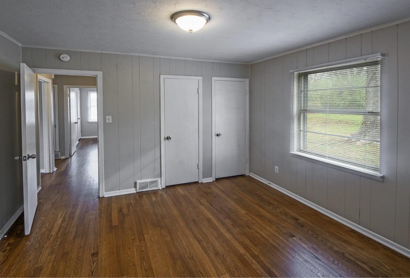 Unfurnished bedroom with dark wood finished floors, ornamental molding, a textured ceiling, wood walls, and multiple closets