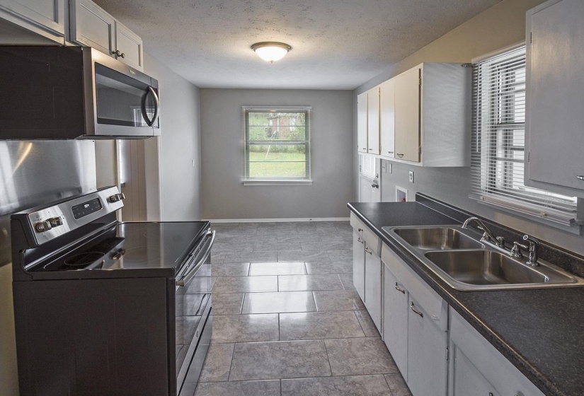Kitchen featuring appliances with stainless steel finishes, dark countertops, white cabinets, and a textured ceiling