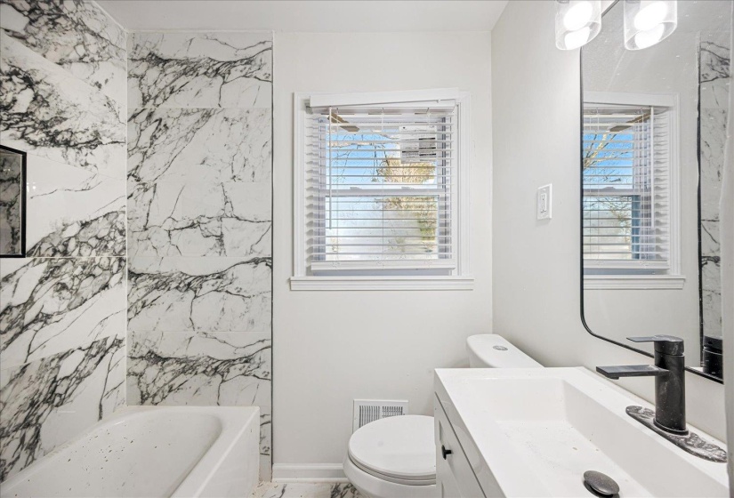 Bathroom featuring a white bathtub, a floating vanity with an integrated sink, a dark-toned faucet, and a large wall mirror