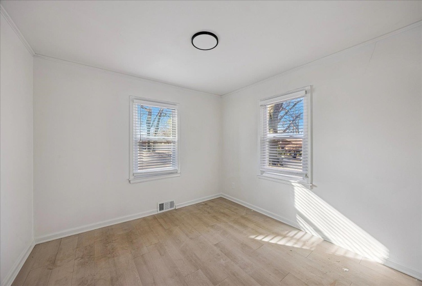 Room featuring light wood-finish flooring, two large windows with blinds, a ceiling-mounted flush light fixture, and white painted walls
