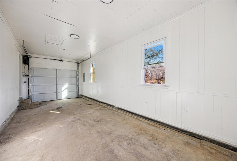 Single-car garage featuring a concrete floor, white paneling, two windows, and an overhead garage door
