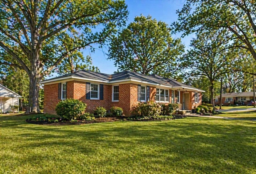 Brick ranch-style residence featuring a dark shingle roof, white trim, and dark window shutters