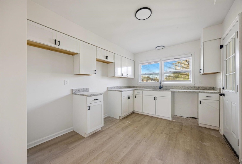 Bright kitchen featuring white cabinetry, light-toned wood-finish flooring, and speckled countertops