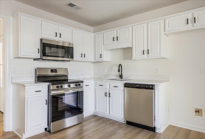 Kitchen featuring white cabinetry, stainless steel appliances, wood-finish flooring, white countertops, and a black gooseneck faucet