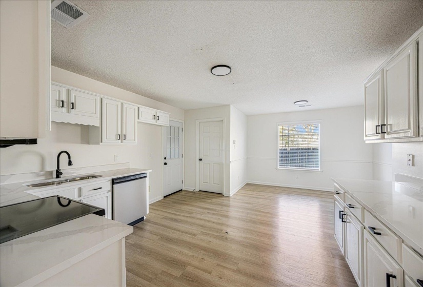 Modern kitchen and dining area featuring light wood-finish flooring, white cabinetry with black hardware, white countertops, a black electric range, and a stainless steel dishwasher