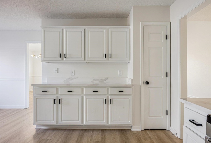 White cabinetry with black hardware, light-toned countertops, and wood-finish flooring