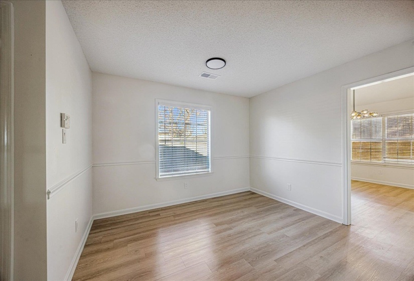 Interior room featuring wood-finish flooring, white walls with chair rail molding, and a single window with horizontal blinds