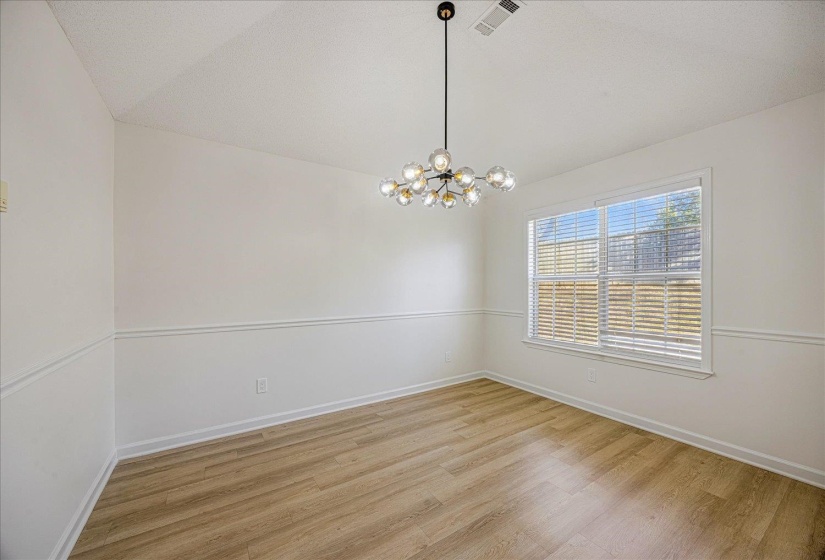 Bright interior space featuring light wood-finish flooring, white walls with decorative chair rail molding, and a modern multi-bulb chandelier